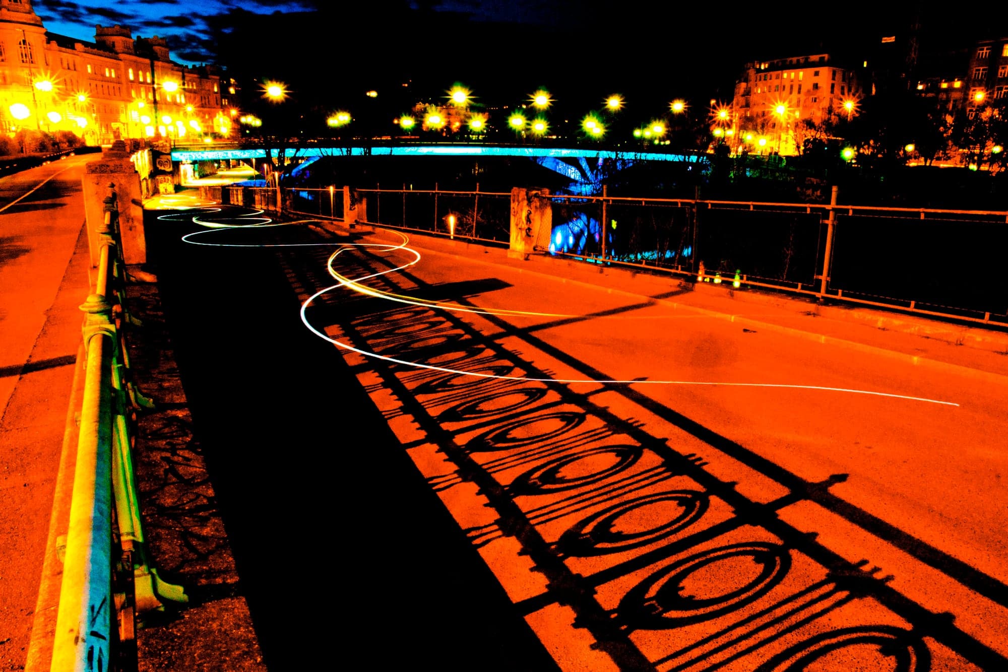 A night street glowing orange, an iron railing's shadow