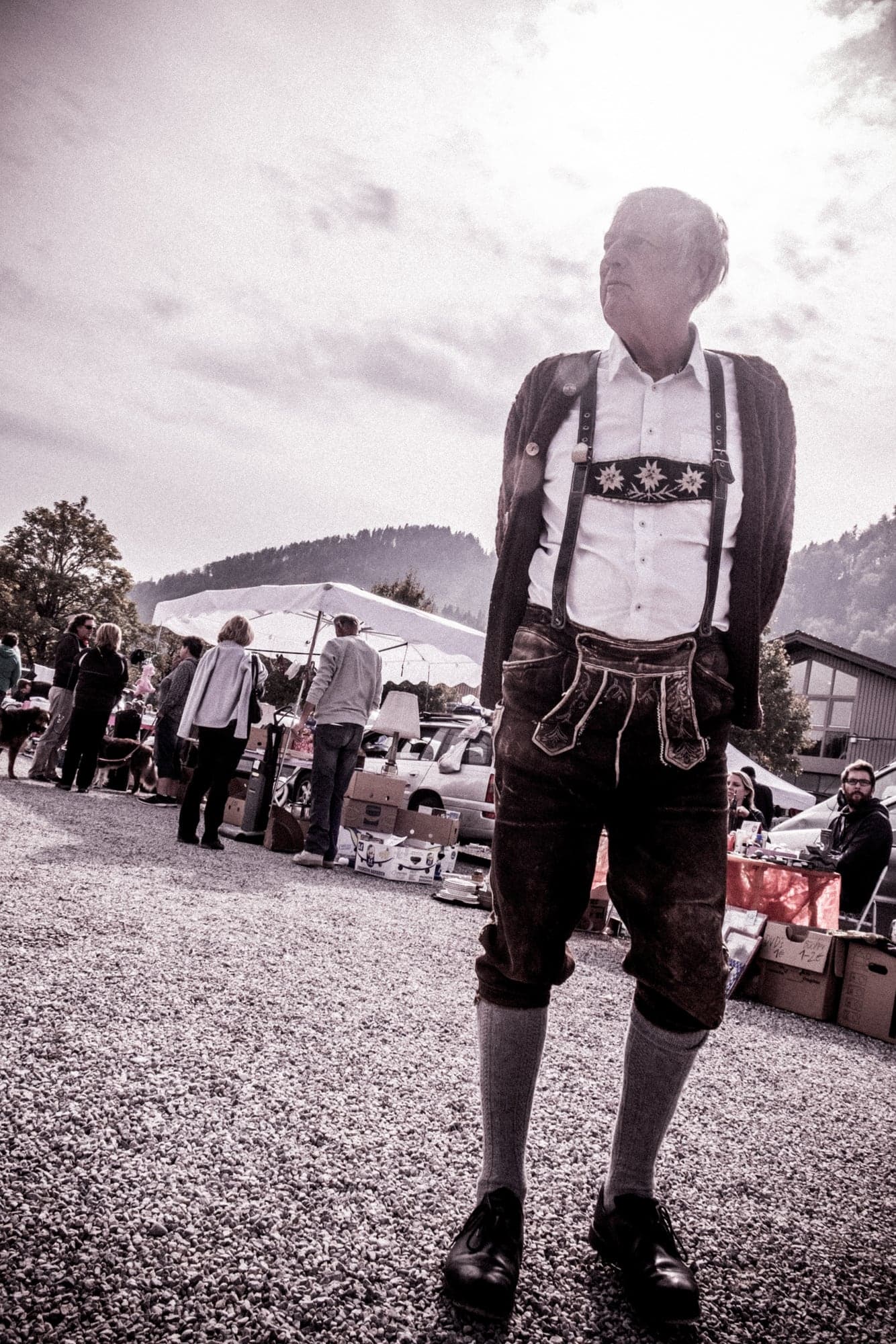 A man in lederhosen at a flea market, in black and white