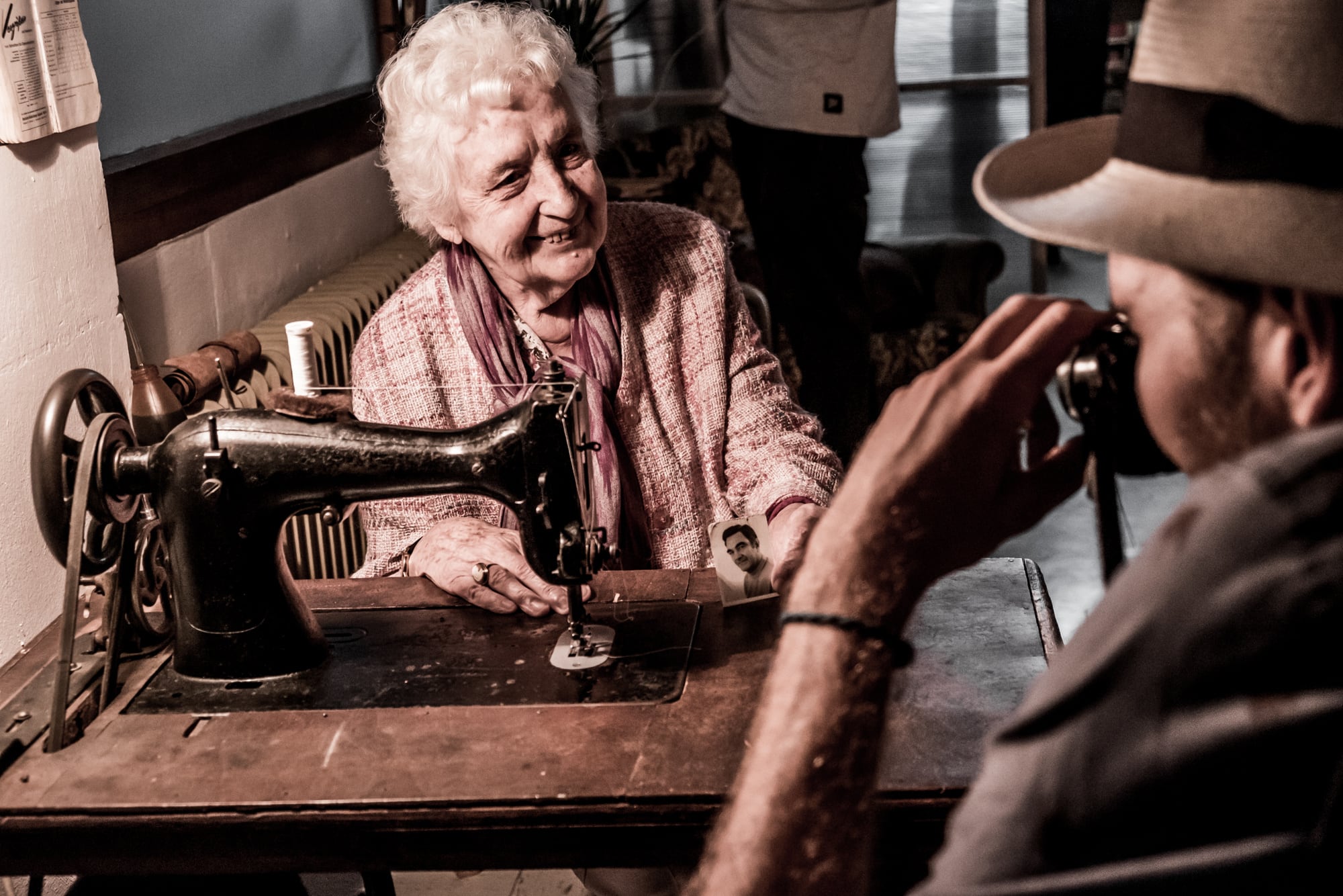 Eine alte Frau an ihrer Nähmaschine, ein Mann fotografiert sie