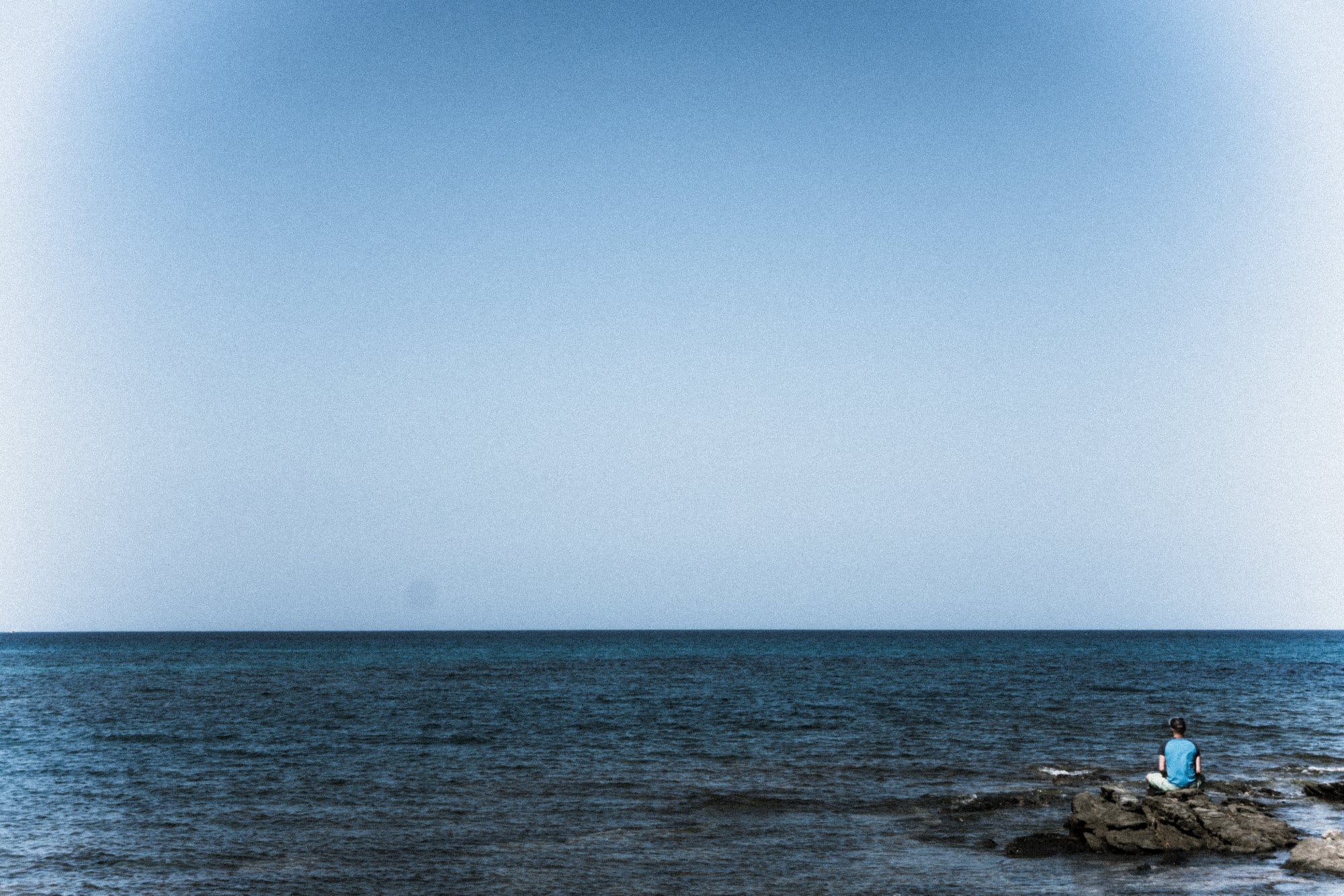 Das Meer trifft auf einen blassen Himmel, Felsen darunter