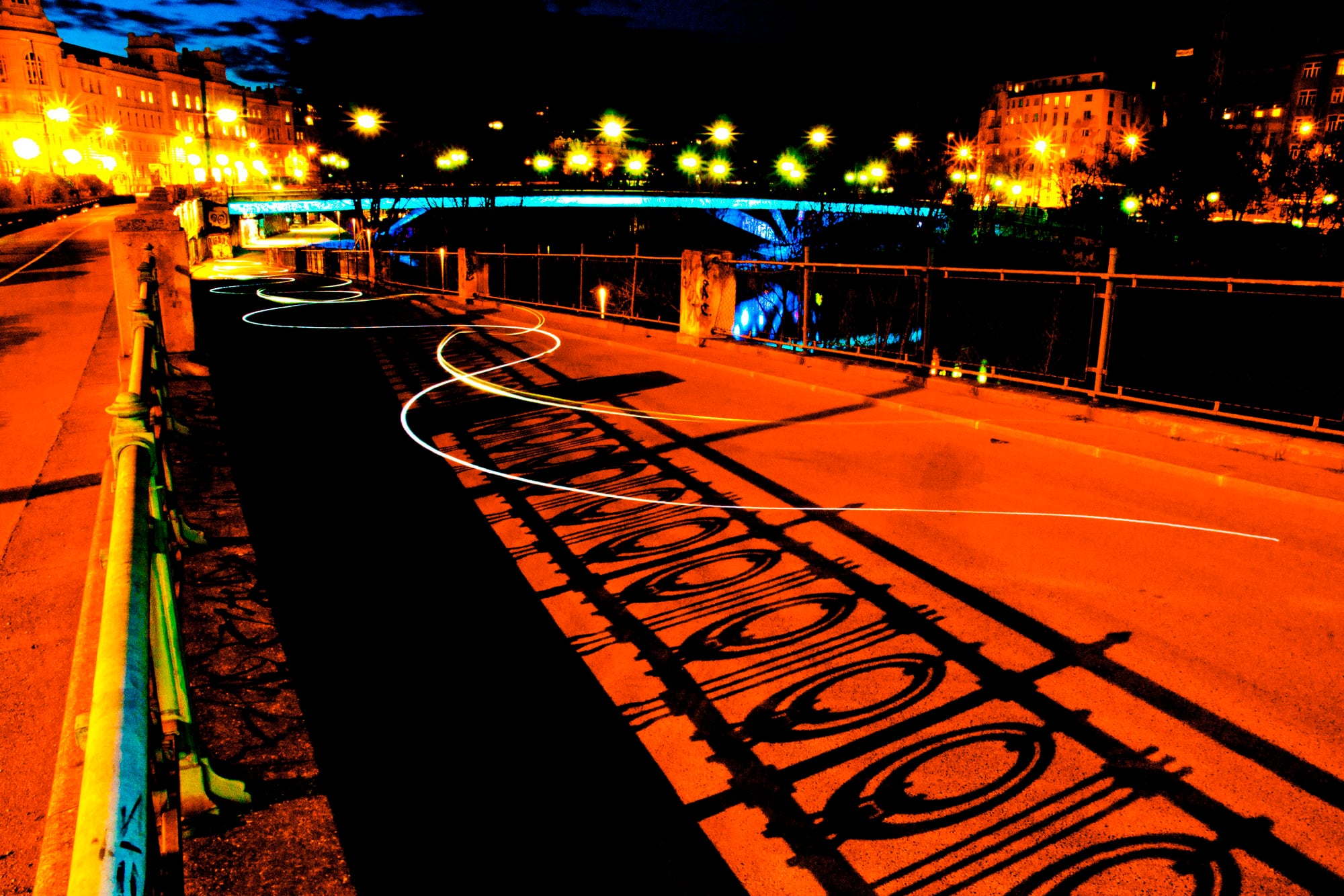 Eine nächtliche Straße glüht orange, der Schatten eines Eisengeländers